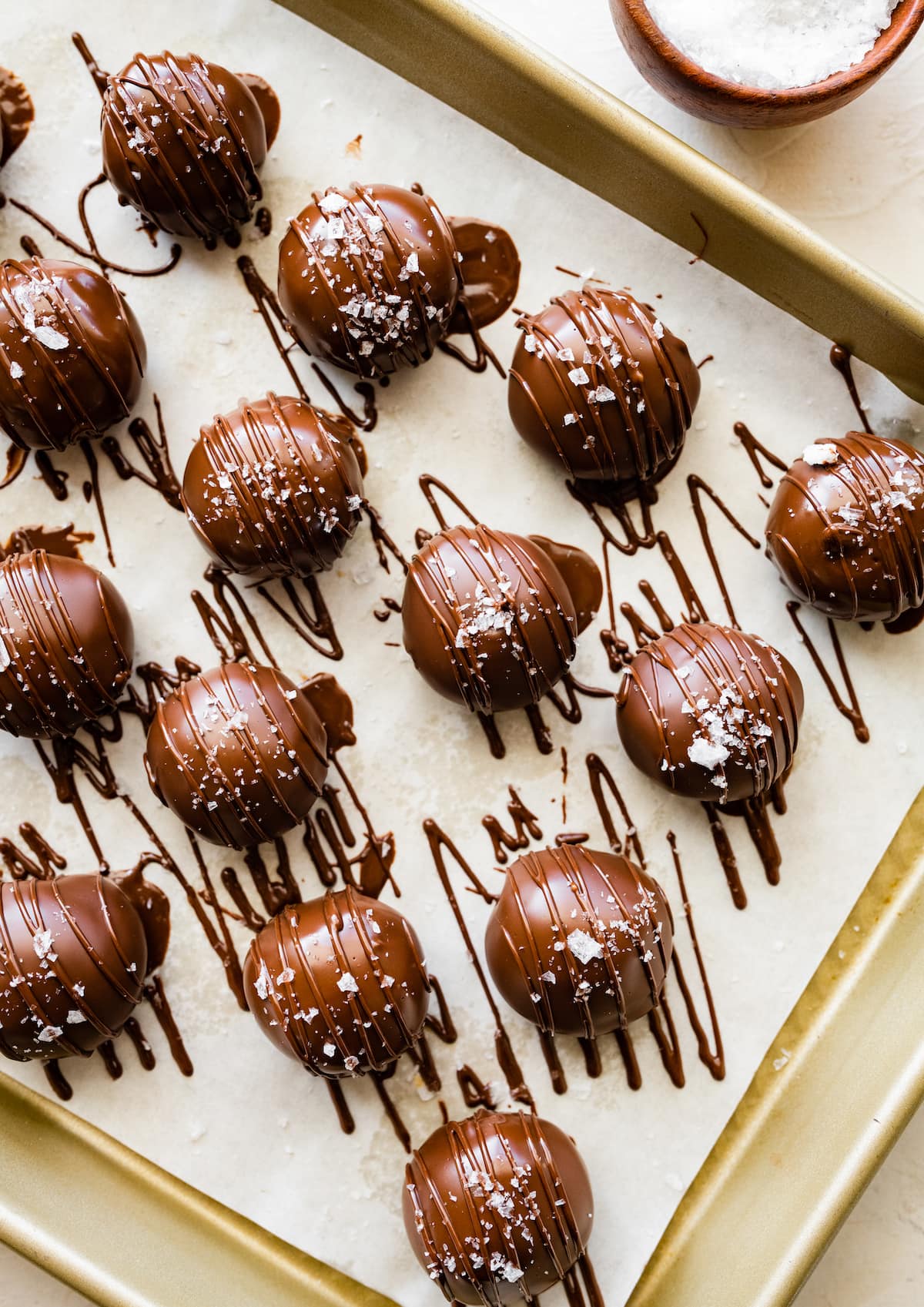 peanut butter protein balls dipped in chocolate and sprinkled with flaky sea salt on baking sheet with parchment paper. 