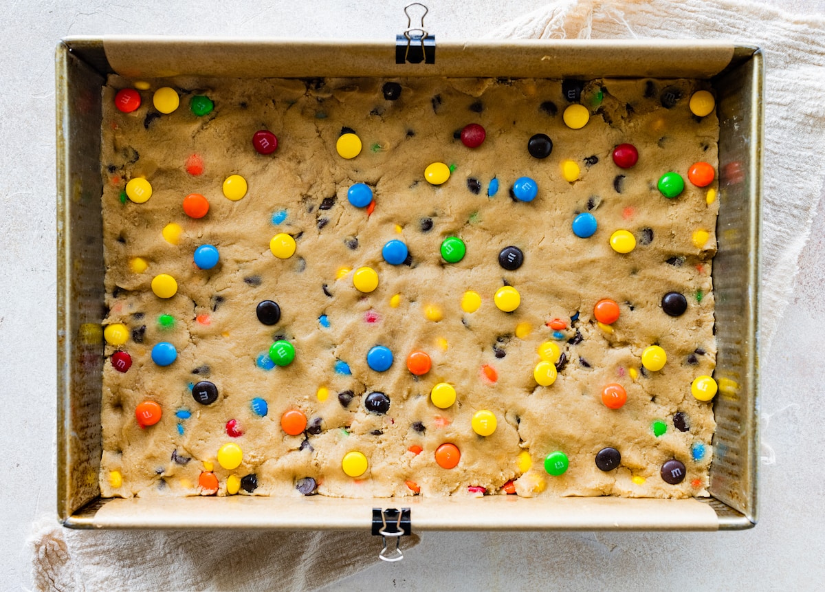 M&M cookie bar dough pressed in pan with parchment paper.