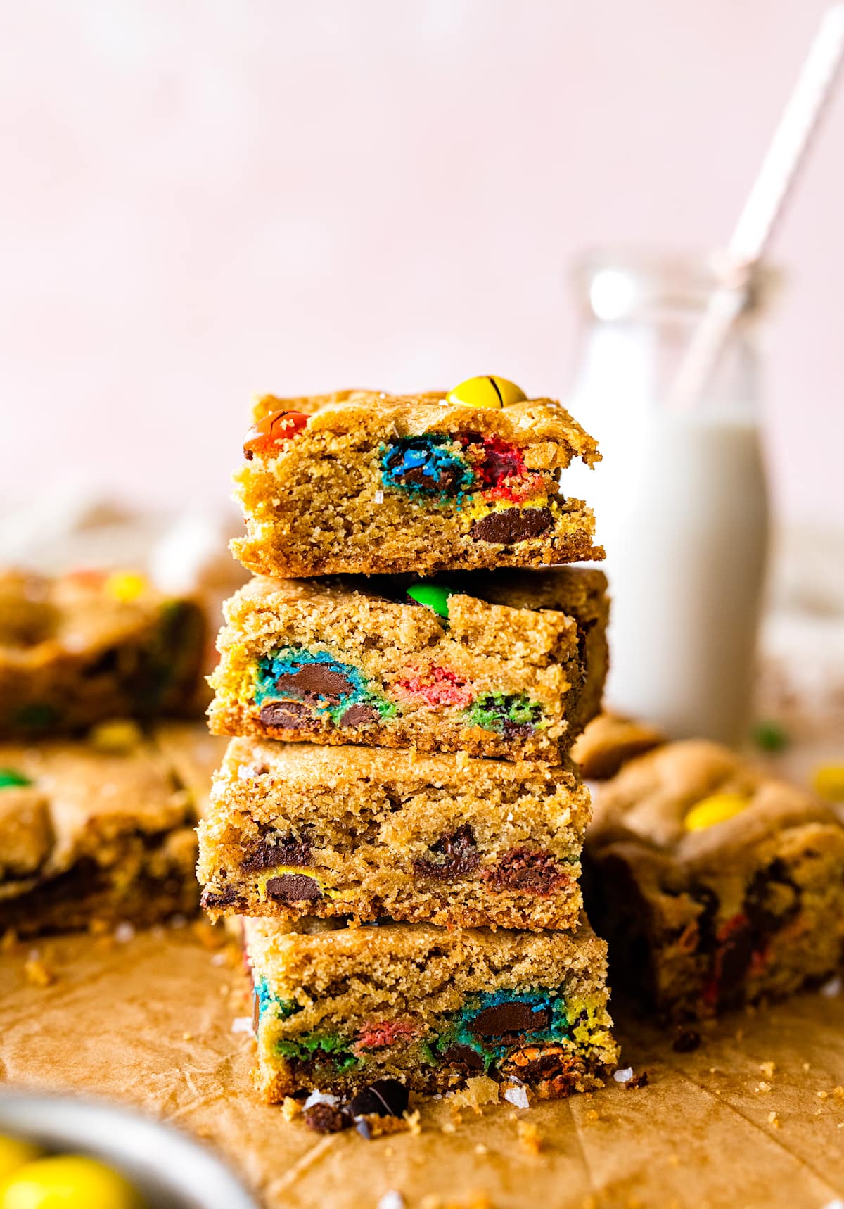 M&M cookie bars cut in squares and stacked on top of each other with bottle of milk. 