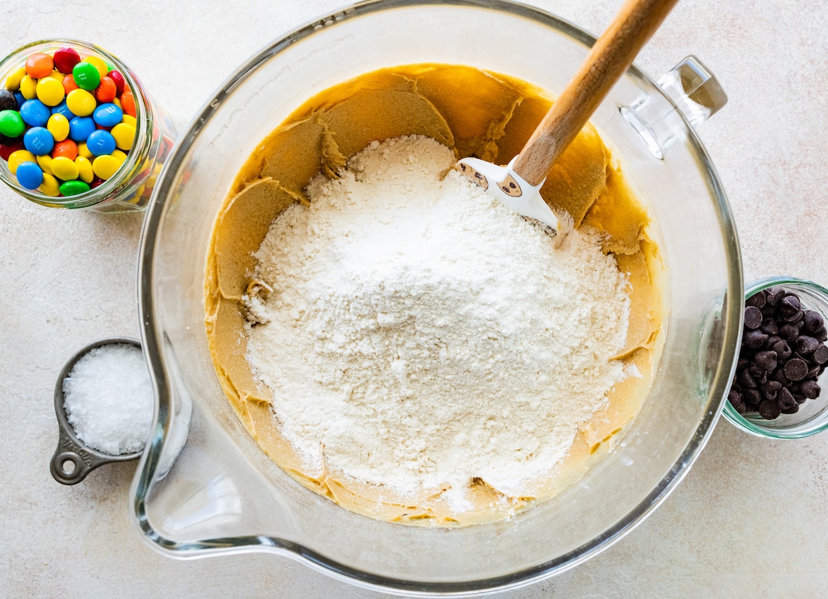 adding dry ingredients to wet ingredients in mixing bowl with spatula. 