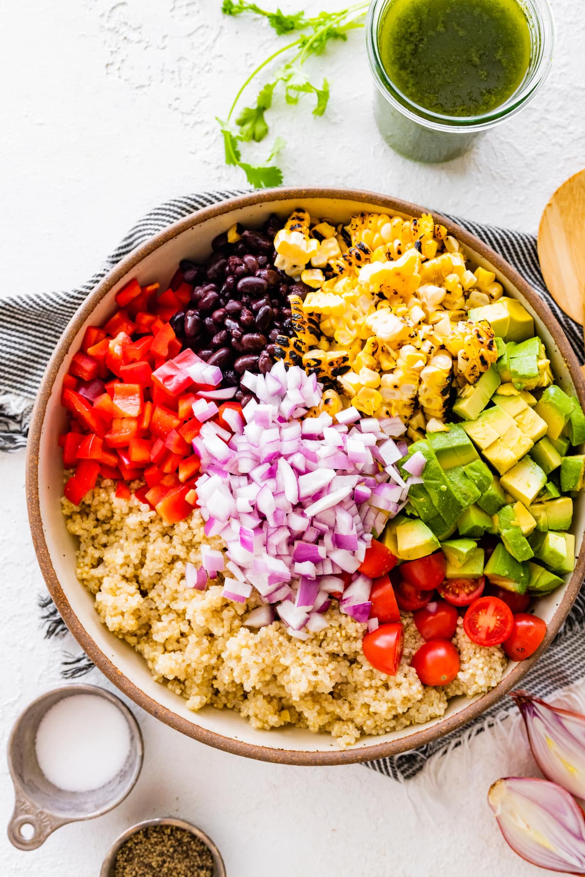 quinoa with red onion, tomatoes, red pepper, black beans, corn, and avocado in large bowl.