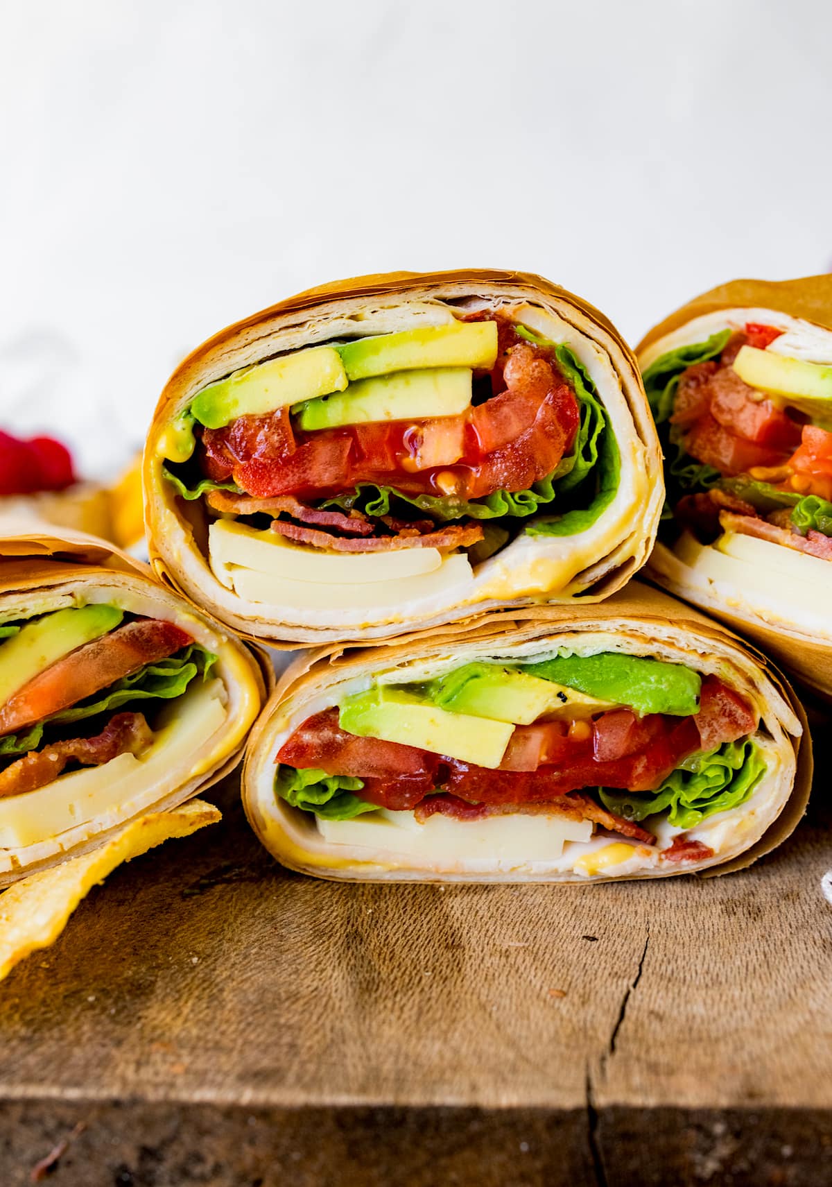 turkey wraps with avocado, tomato, lettuce, bacon, and cheese cut in half and stacked on wood cutting board. 