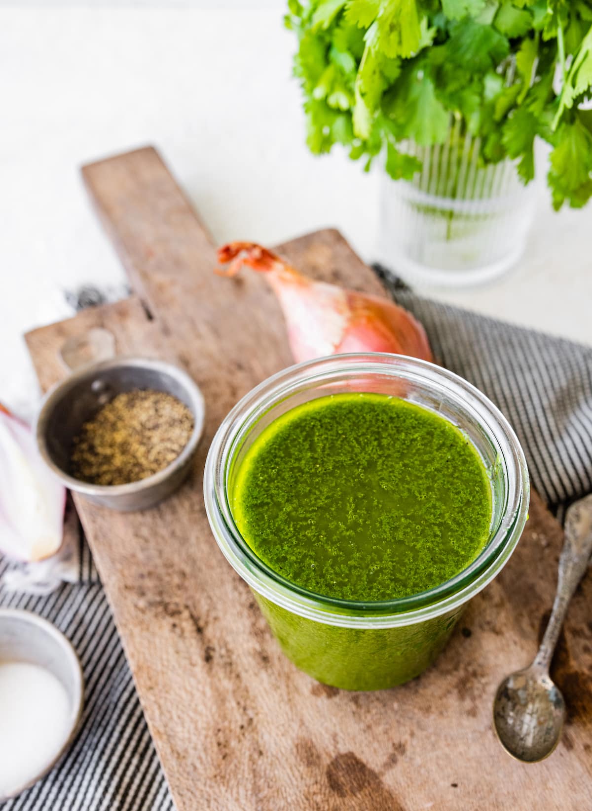 cilantro lime vinaigrette in glass jar on wood board with spoon on side. 