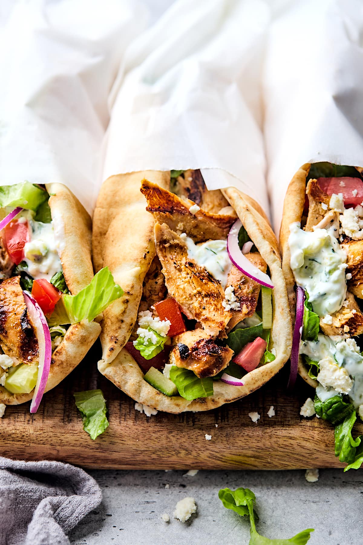 chicken gyros wrapped in white paper on wood cutting board. 