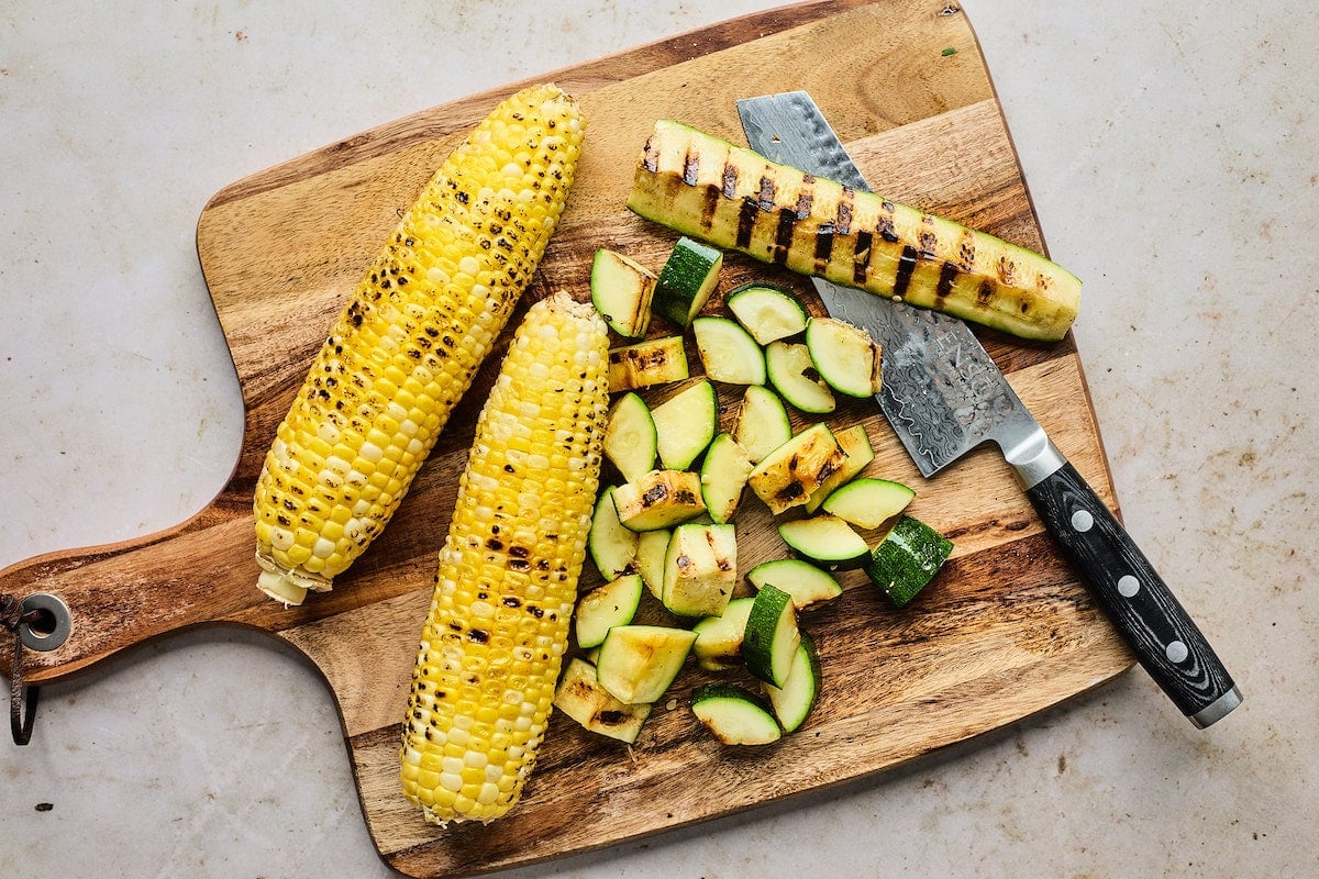 grilled corn and zucchini on cutting board with knife. 
