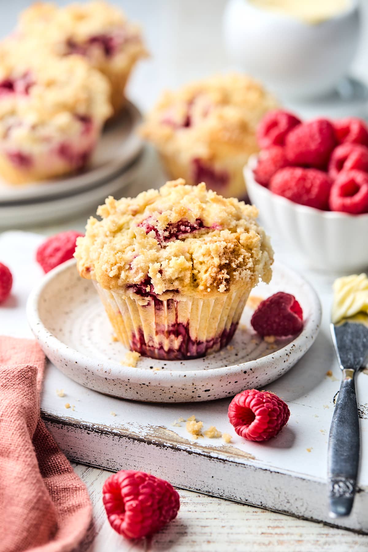 raspberry muffin with streusel topping on plate with fresh raspberries. 