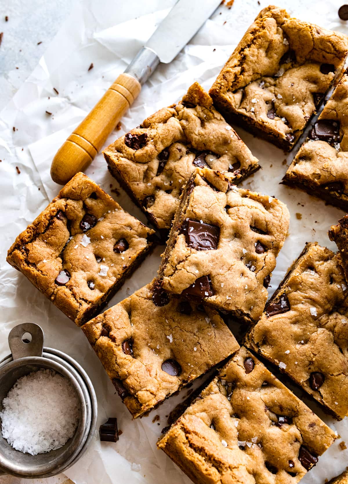 brown butter chocolate chip cookie bars cut into squares on parchment paper with flaky sea salt. 