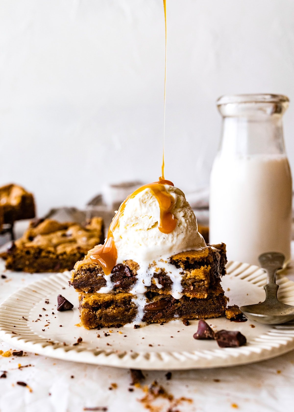 brown butter chocolate chip cookie bars stacked on plate with ice cream and caramel sauce. 