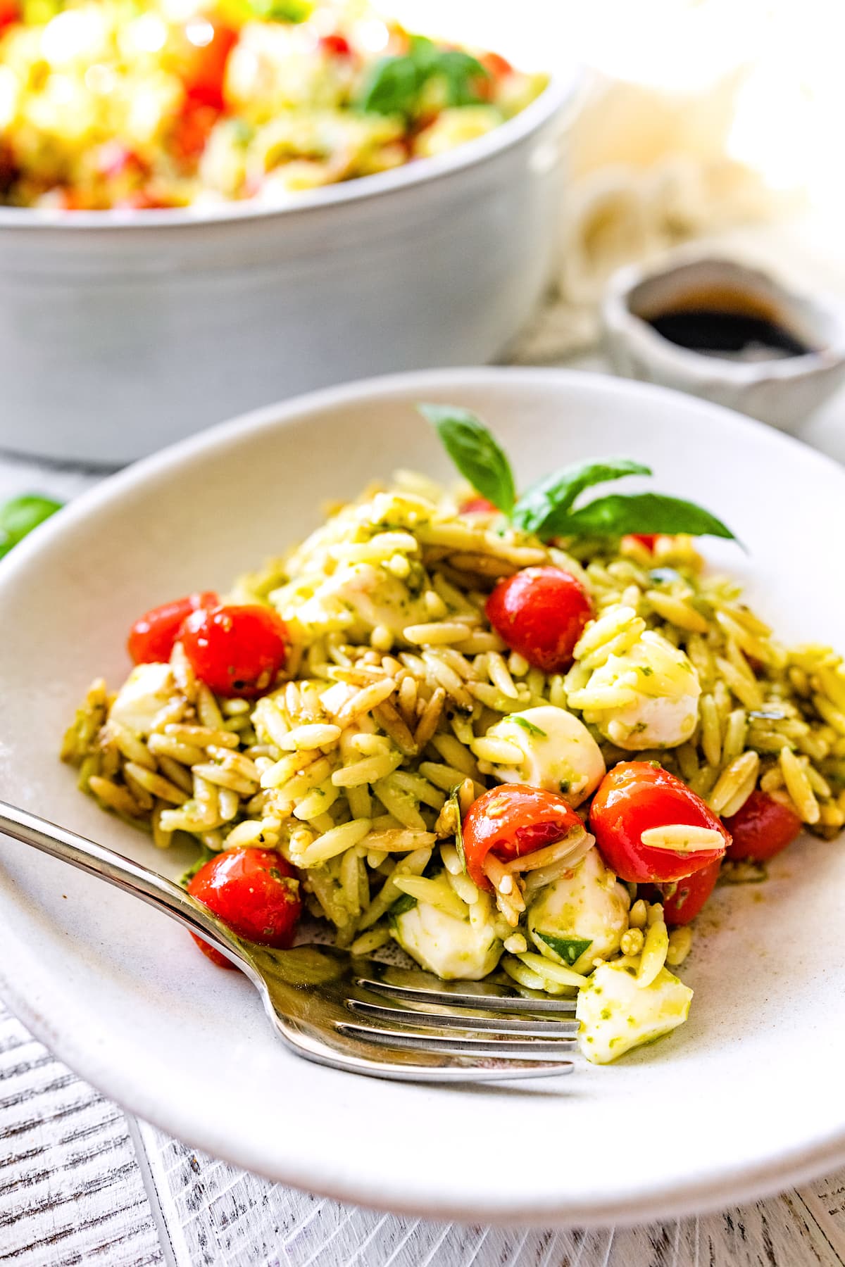 caprese orzo salad on white plate with fork. 