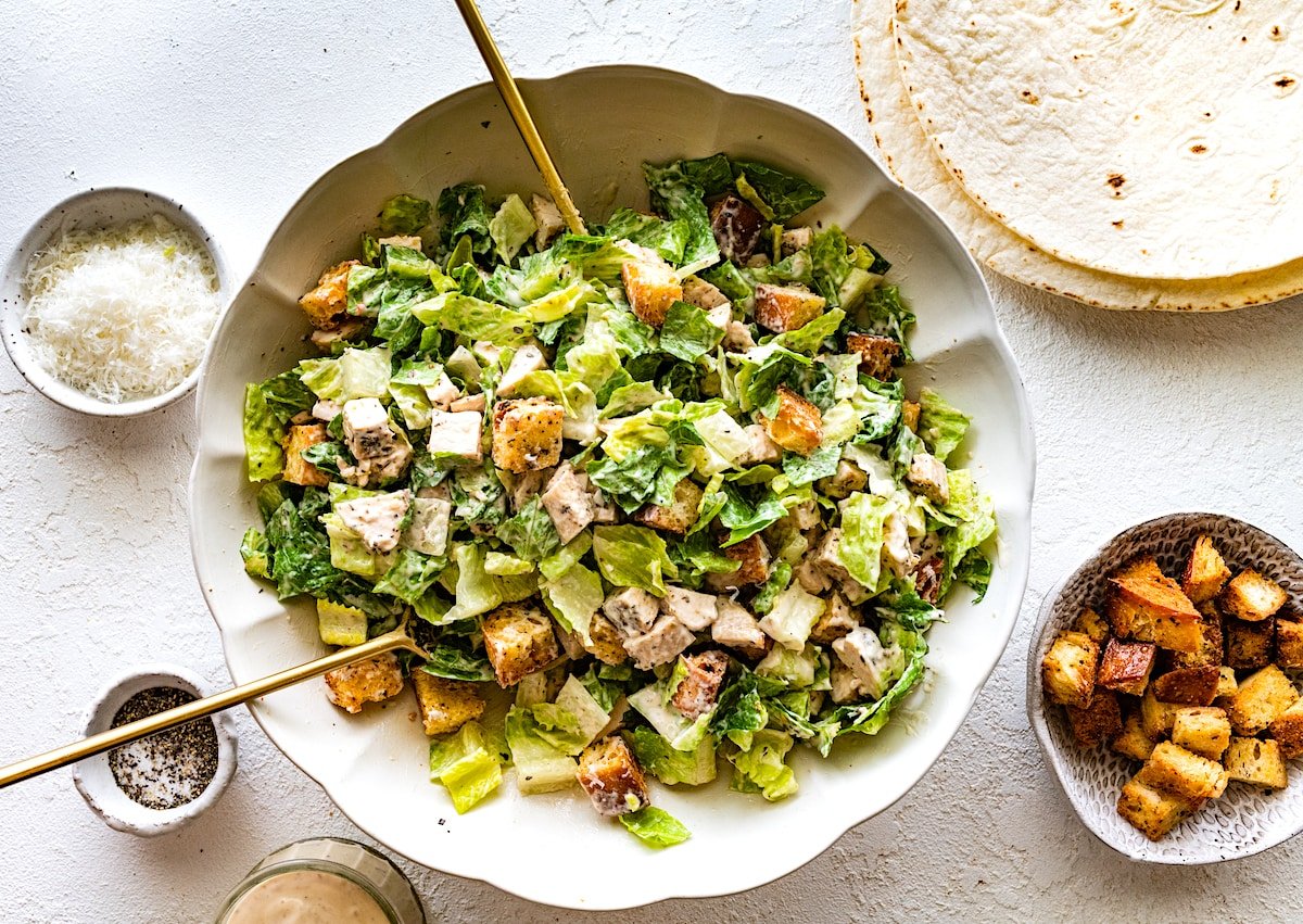 chicken caesar salad in bowl with salad servers. 