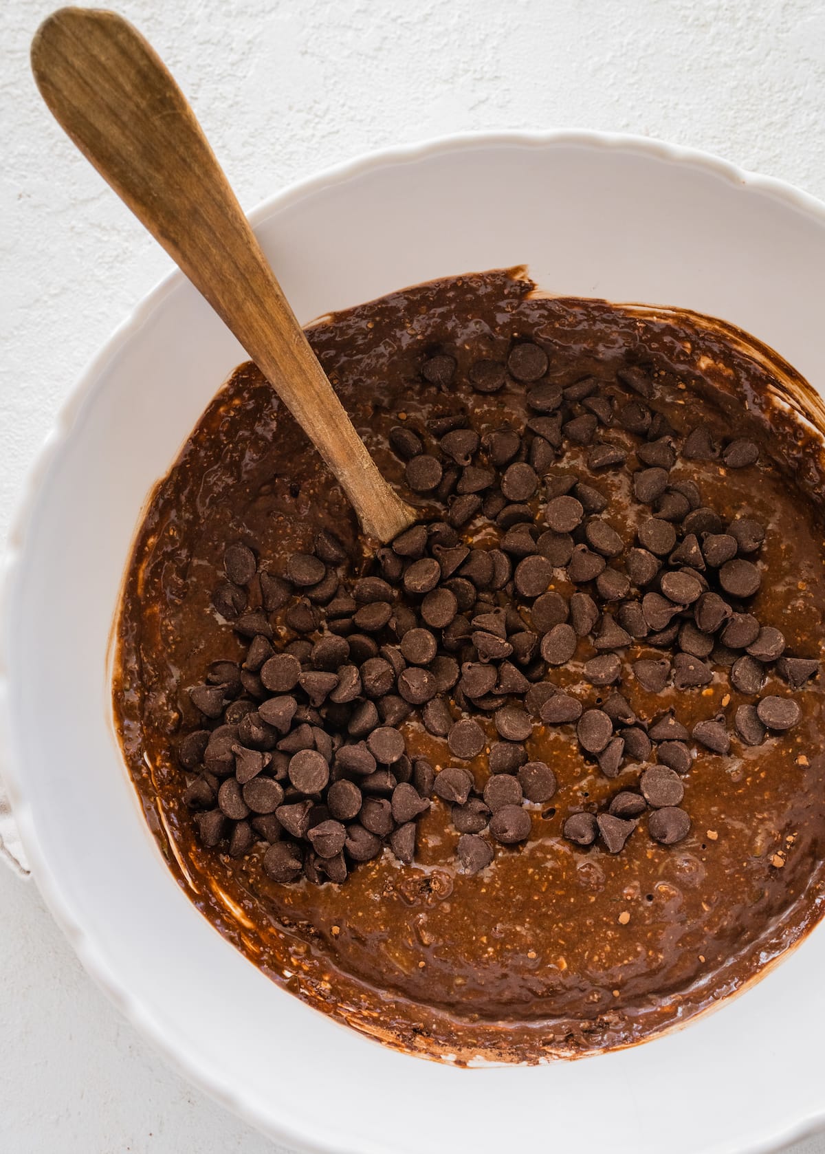 chocolate zucchini snack cake batter with chocolate chips in mixing bowl with spoon. 