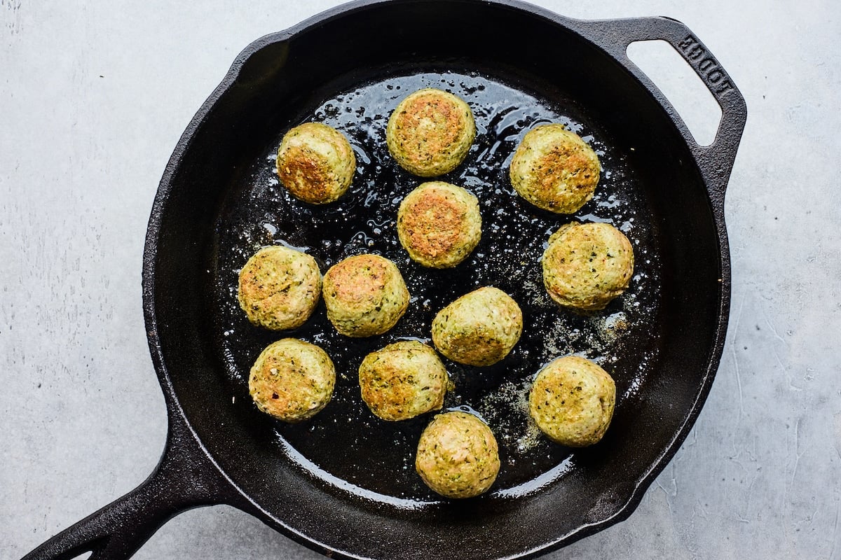 pesto meatballs being cooked in cast iron skillet. 