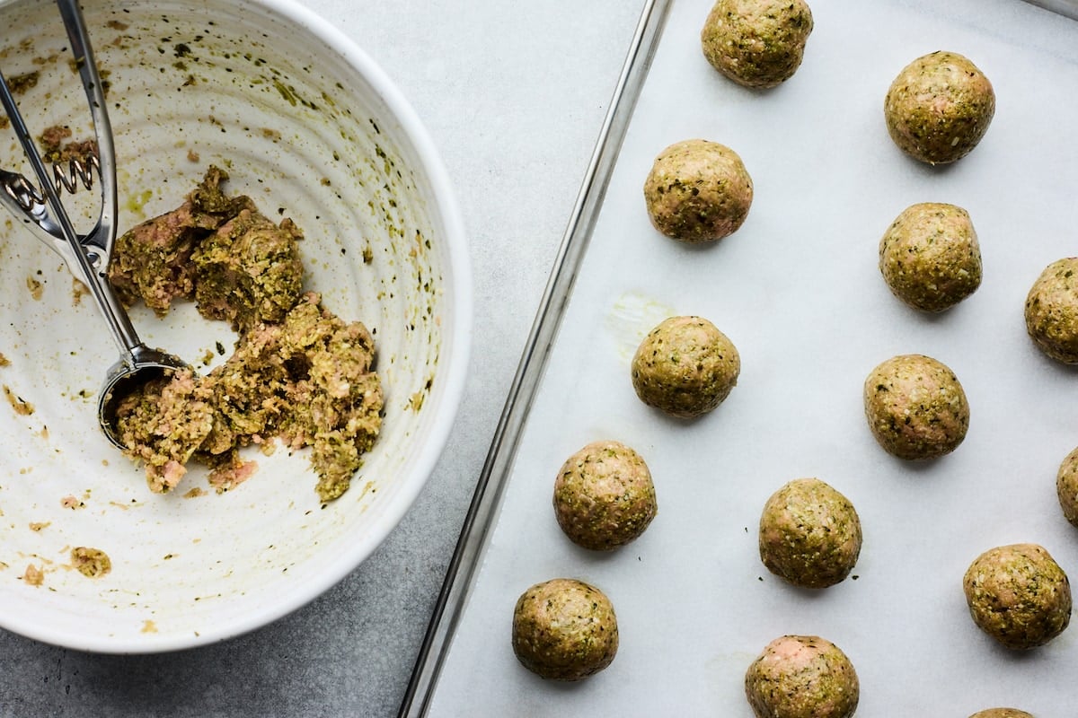 pesto meatballs being scooped onto baking sheet. 