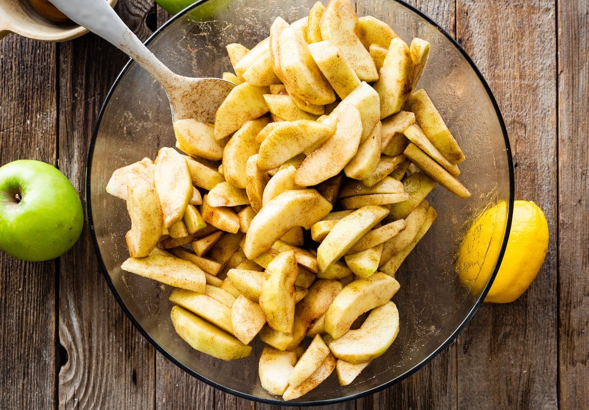 apple slices tossed in cinnamon and sugar in mixing bowl. 