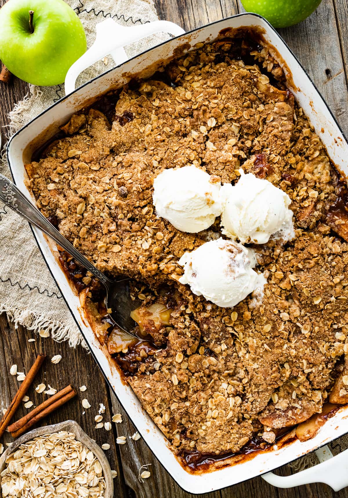apple crisp in pan with three scoops of vanilla ice cream and serving spoon. 