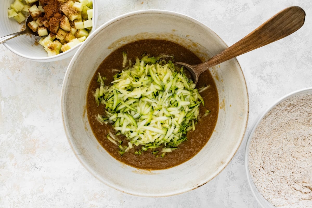 apple zucchini bread batter in mixing bowl with the zucchini being stirred in. 