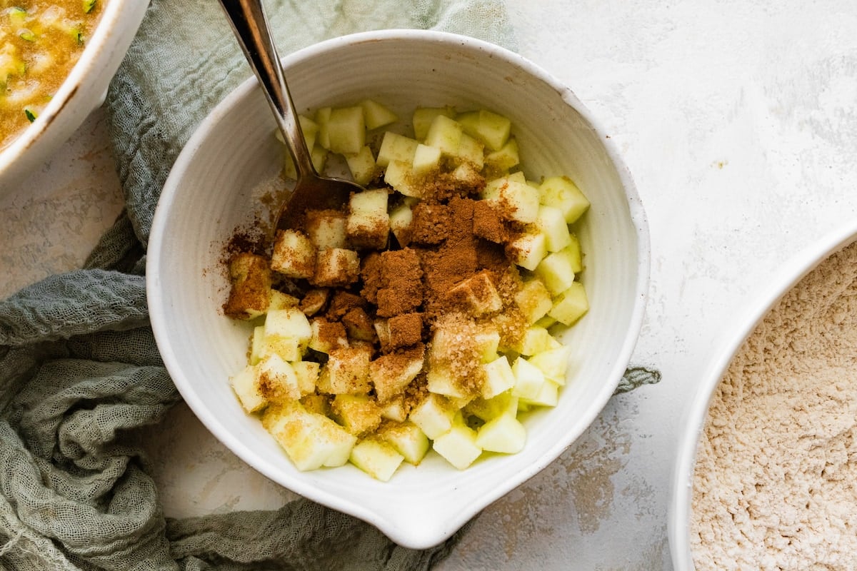 chopped apples with cinnamon and sugar in mixing bowl with spoon. 