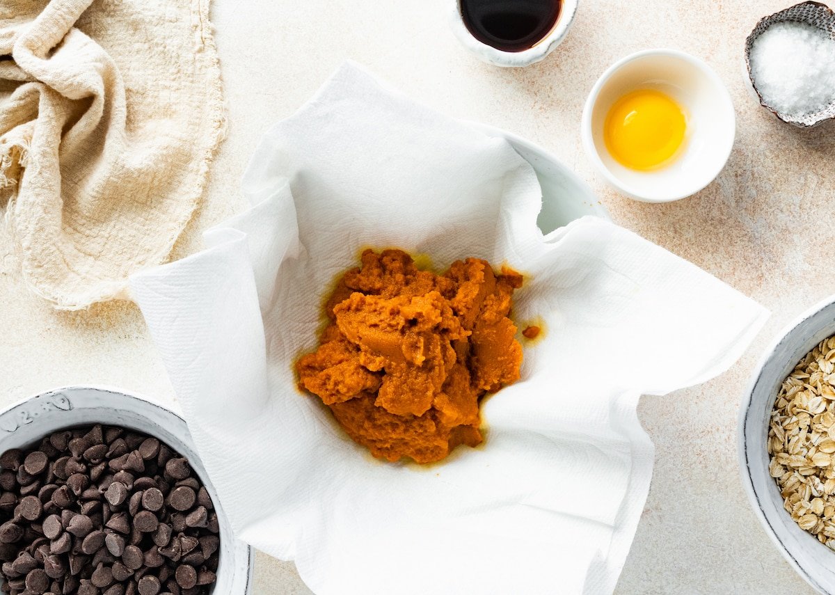 pumpkin puree being blotted in paper towels to make pumpkin oatmeal chocolate chip cookies. 