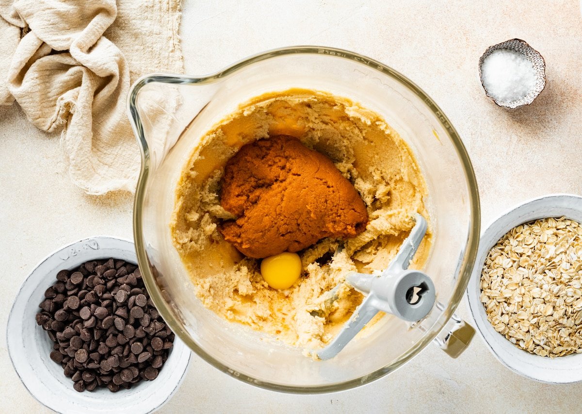 creaming butter, sugars, eggs, and pumpkin in mixing bowl to make pumpkin oatmeal chocolate chip cookies. 