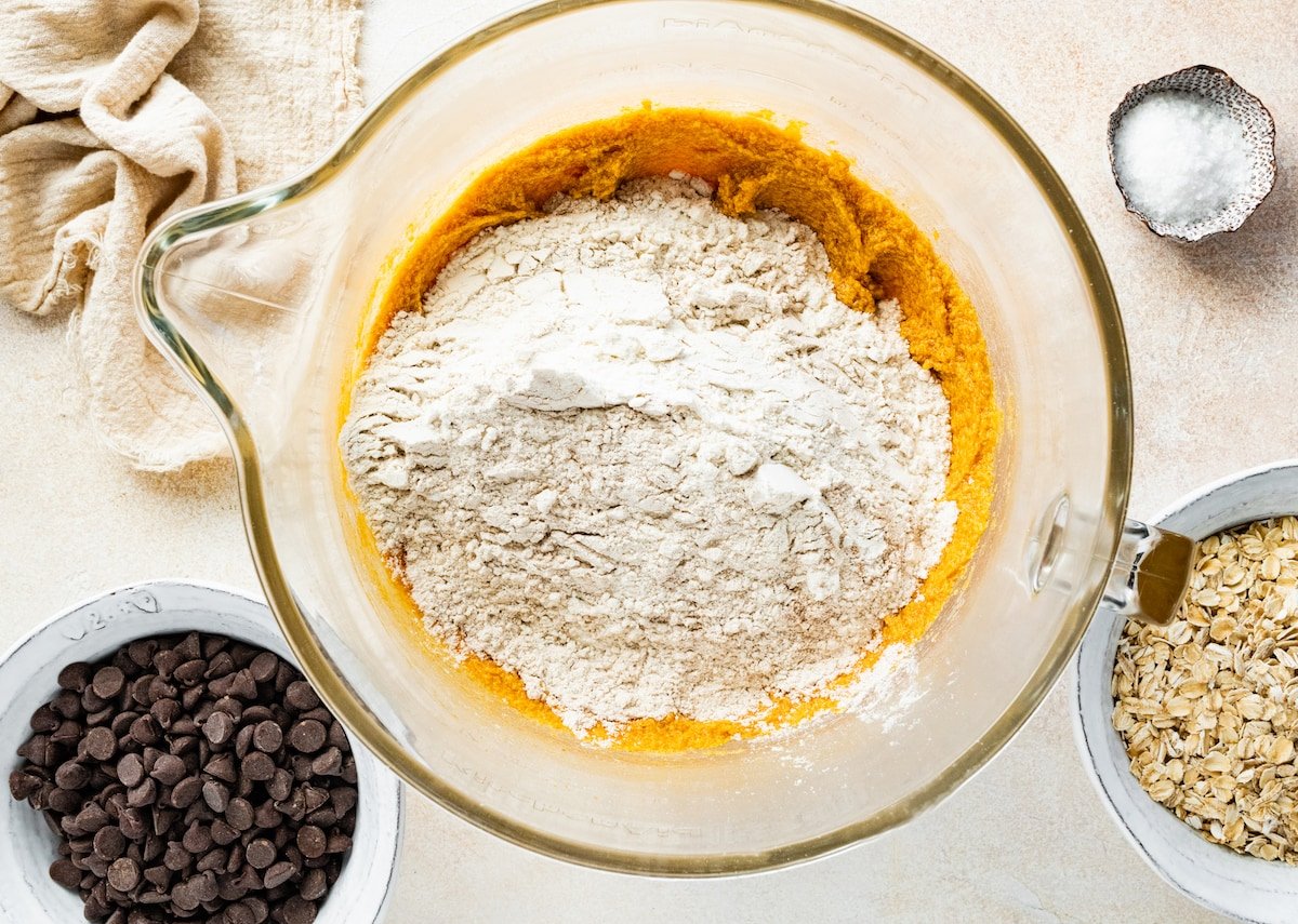 dry ingredients being added to pumpkin cookie dough in mixing bowl. 