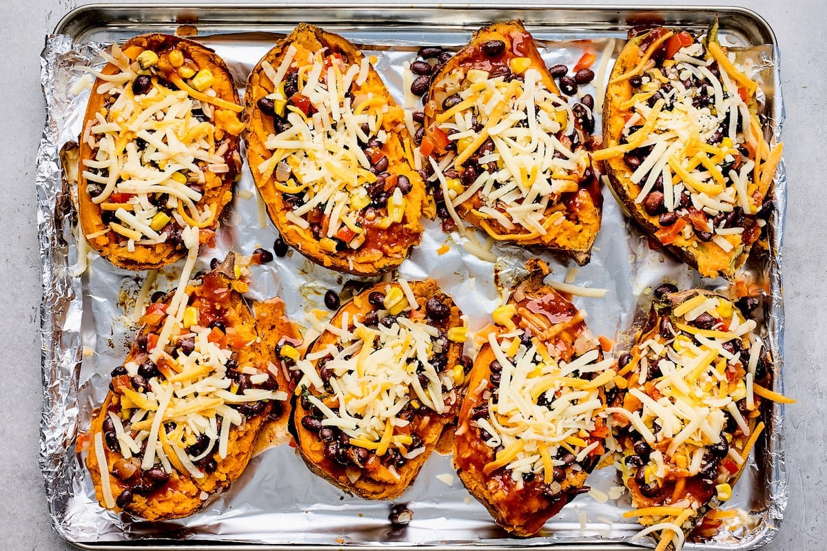 stuffed sweet potatoes on baking sheet with cheese getting ready to be baked in the oven. 