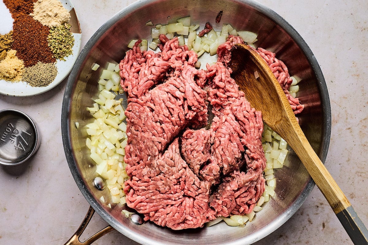 ground beef and onion cooking in skillet with wooden spoon. 