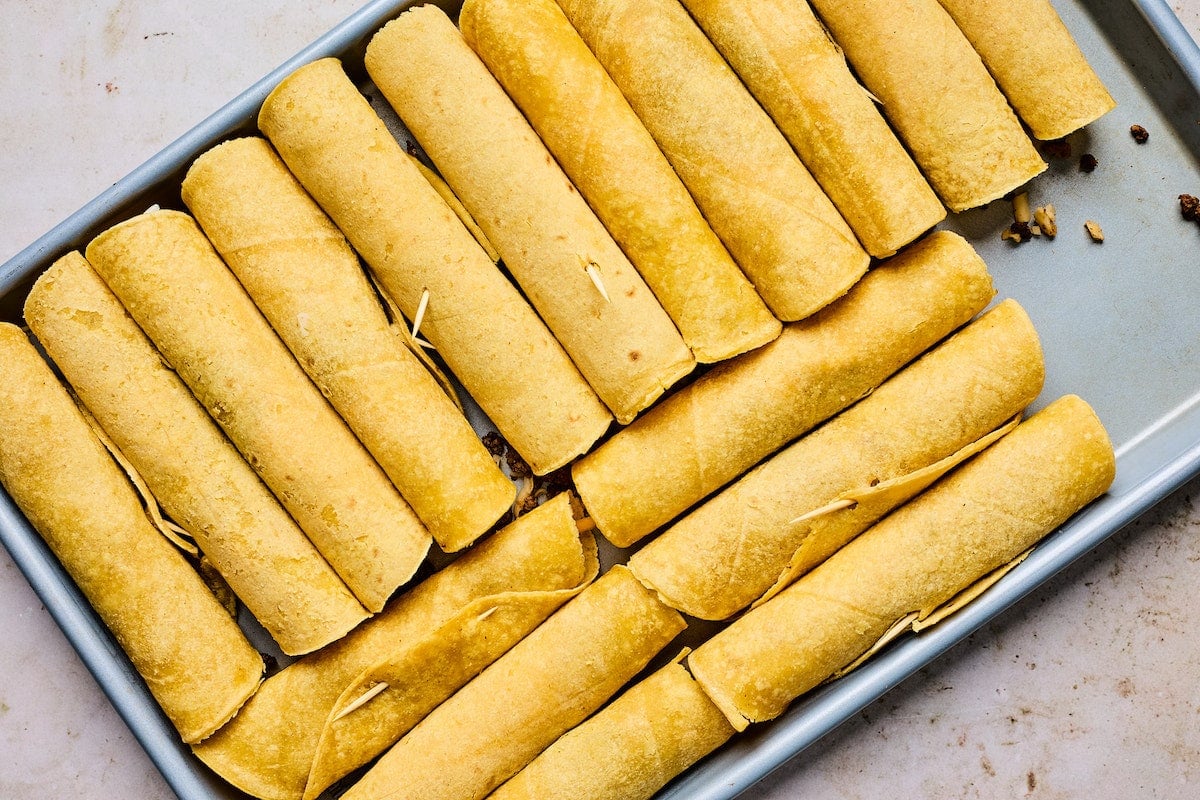 beef taquitos rolled up with toothpicks on baking sheet. 