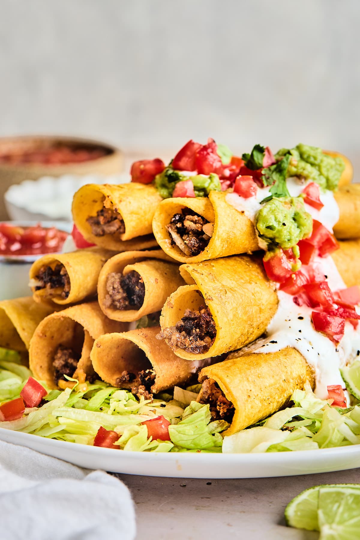 stack of beef taquitos on platter with shredded lettuce and tomatoes. 