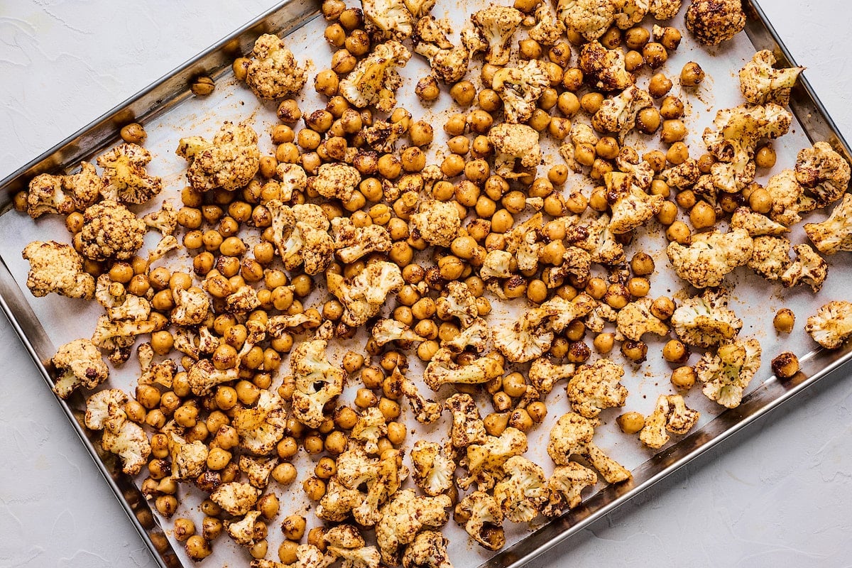 cauliflower and chickpeas tossed in spices on baking sheet with parchment paper. 