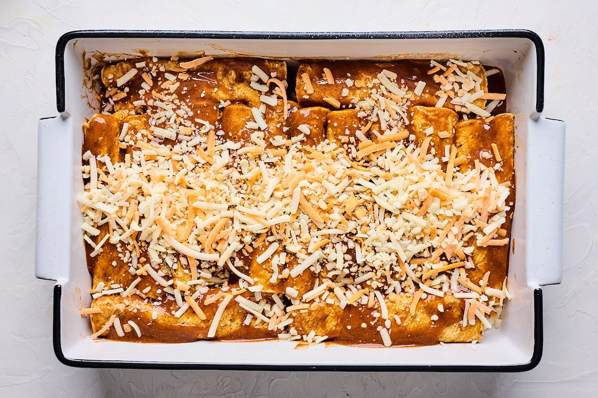 rolled up cauliflower enchiladas in pan with enchilada sauce and shredded cheese. 