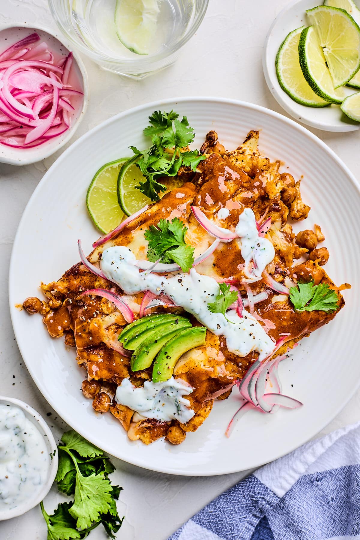 cauliflower enchiladas on plate with lime crema, avocado, red onion, and cilantro. 