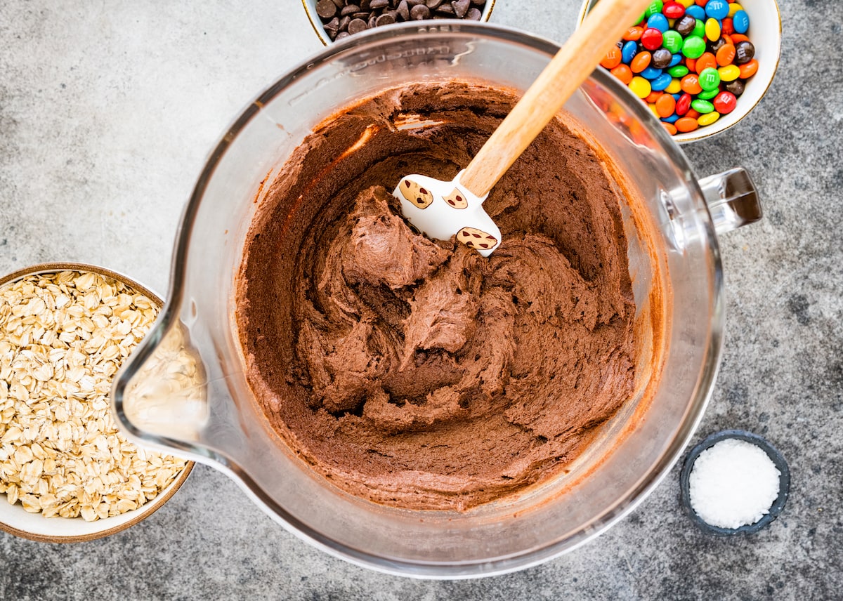 chocolate monster cookie dough in mixing bowl with spatula. 
