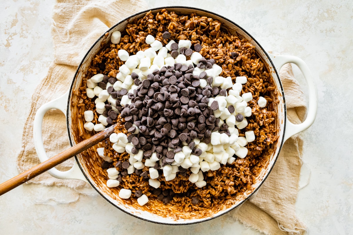 marshmallows and chocolate chips being stirred into chocolate rice krispie treats in a big pot. 