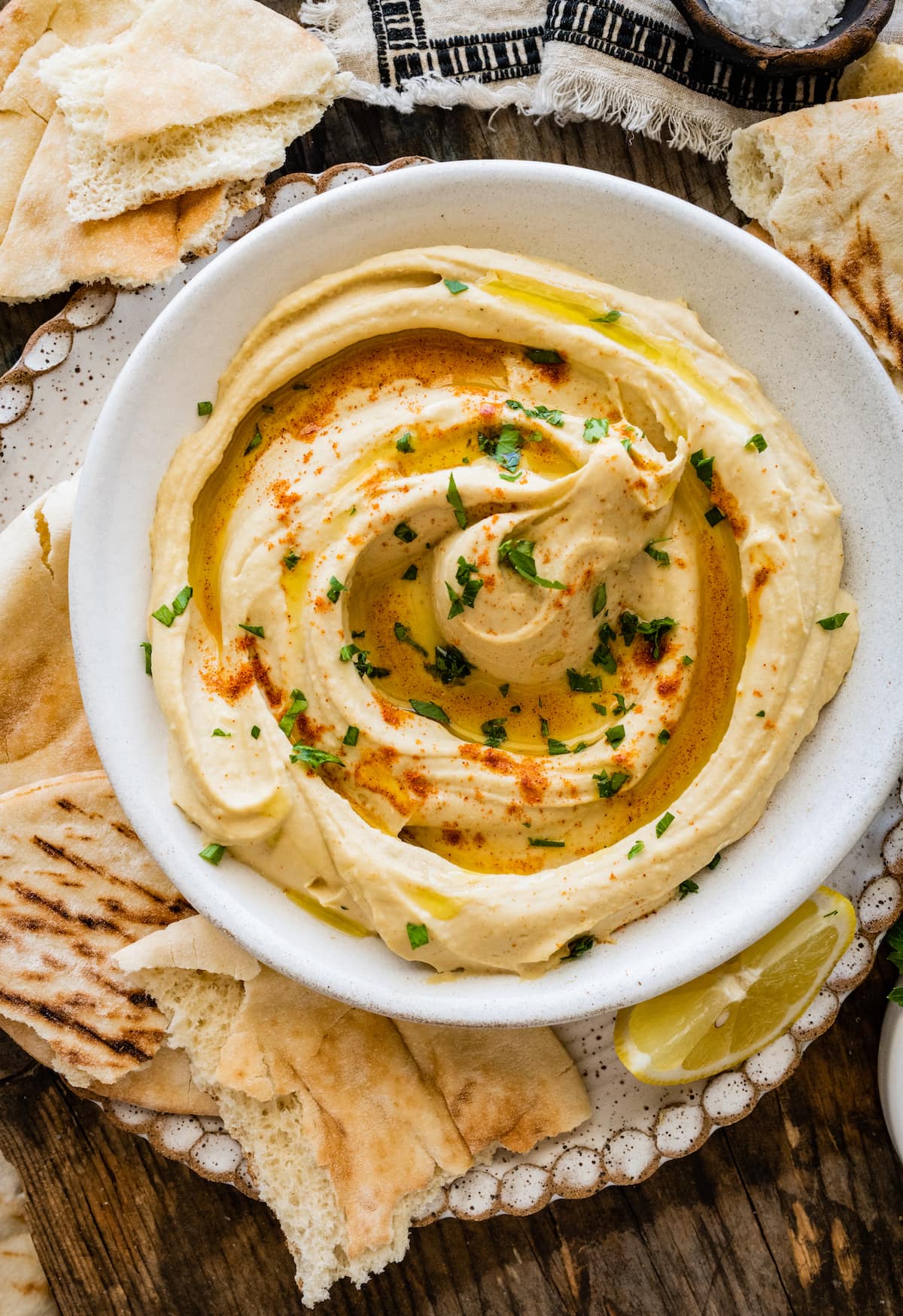 hummus in bowl with olive oil, paprika, and parsley and pita bread. 