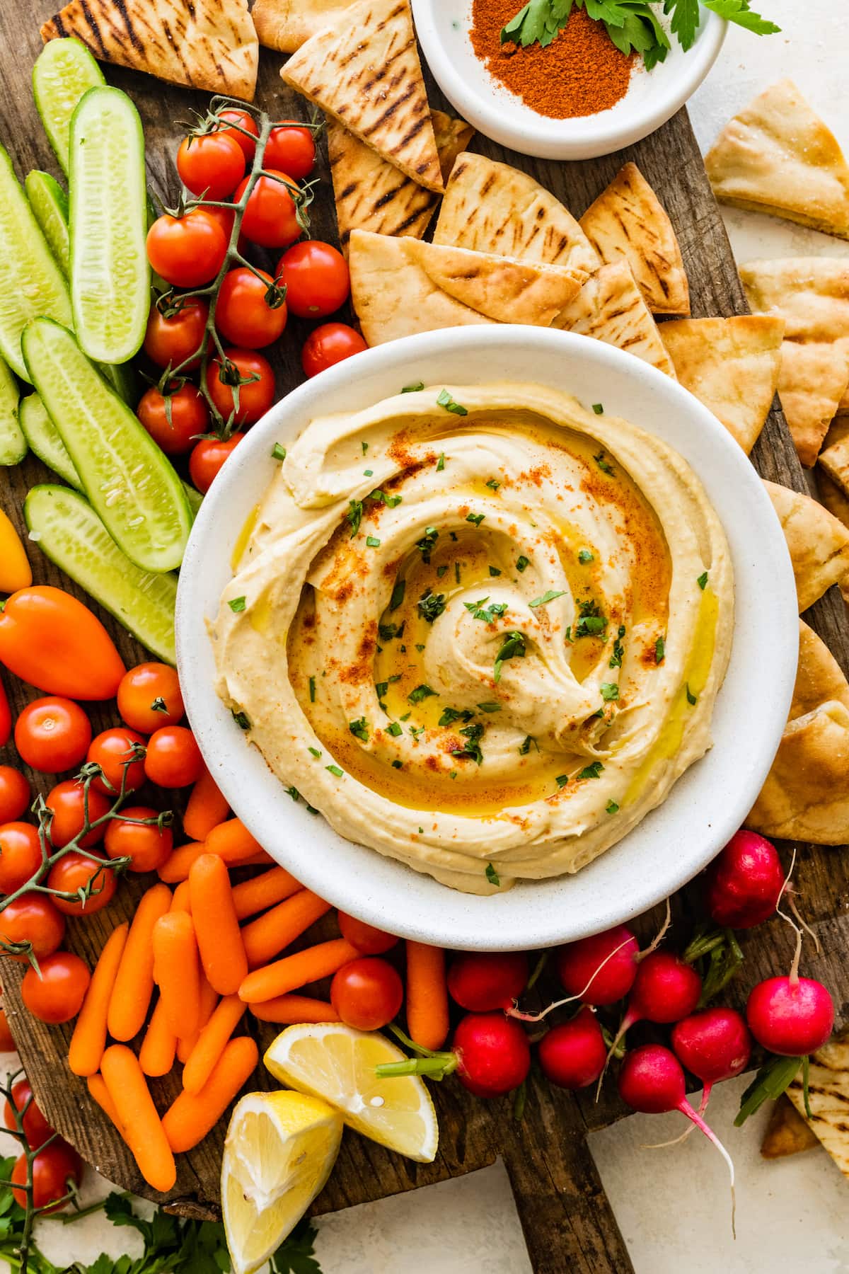 hummus in bowl on wood board with pita chips and vegetables. 