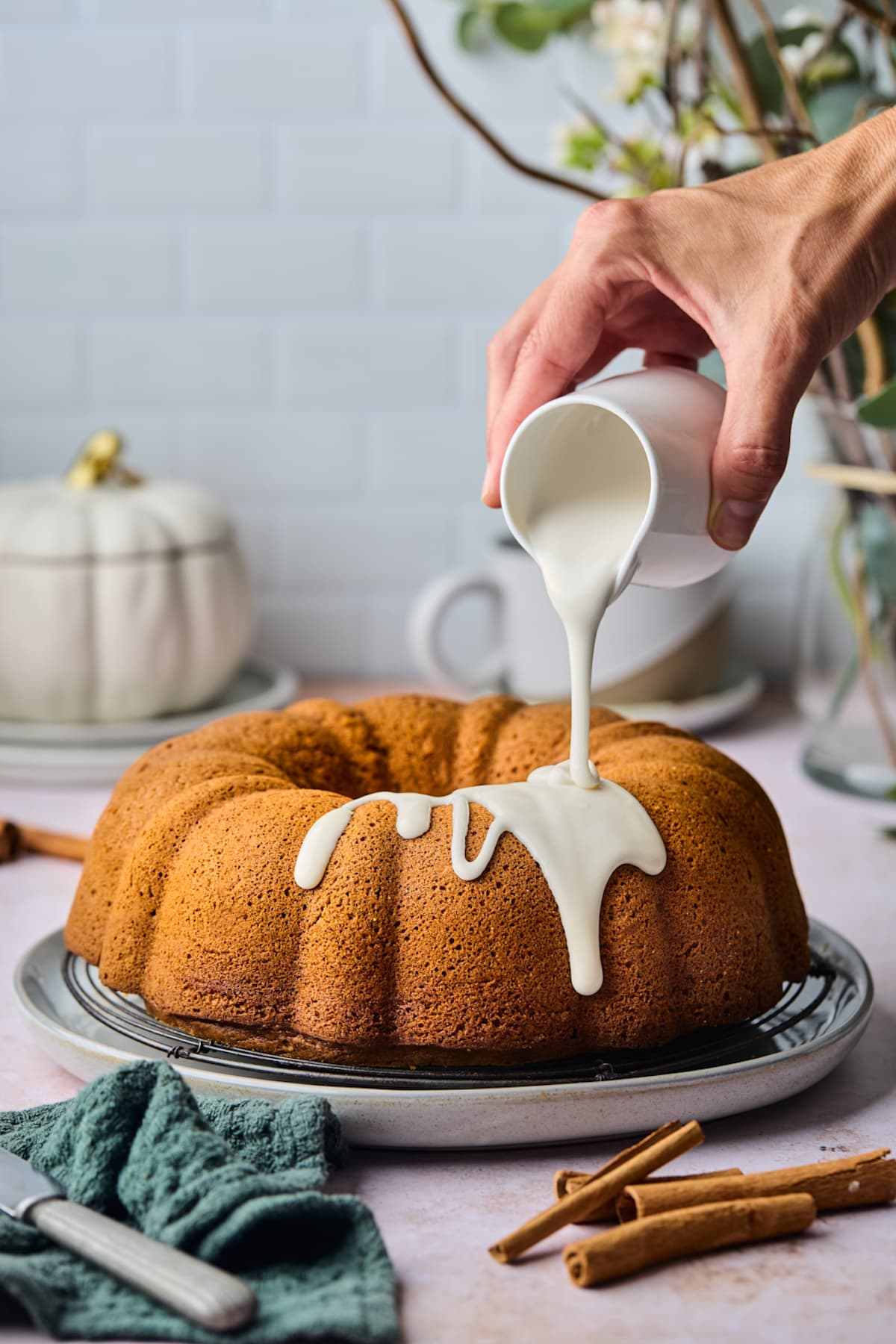 pumpkin bundt cake on cooling rack with cream cheese frosting being poured over the top. 