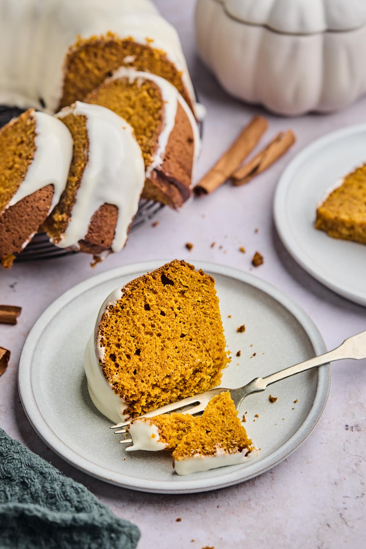 piece of pumpkin bundt cake with cream cheese frosting on plate with fork. 