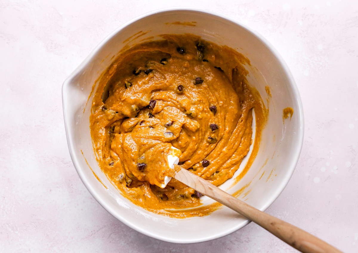 pumpkin chocolate chip muffin batter in mixing bowl with spatula. 