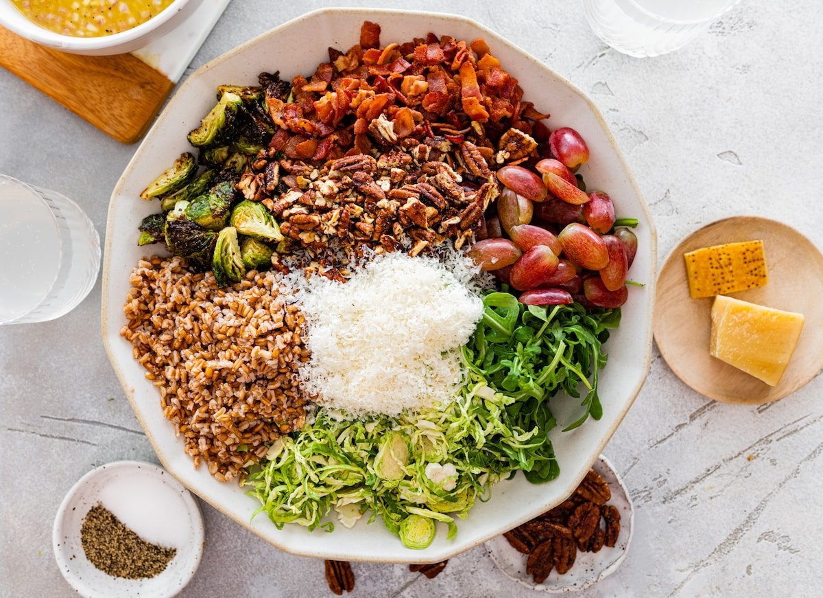 brussels sprouts, arugula, farro, parmesan cheese, grapes, pecans, and bacon in salad serving bowl. 