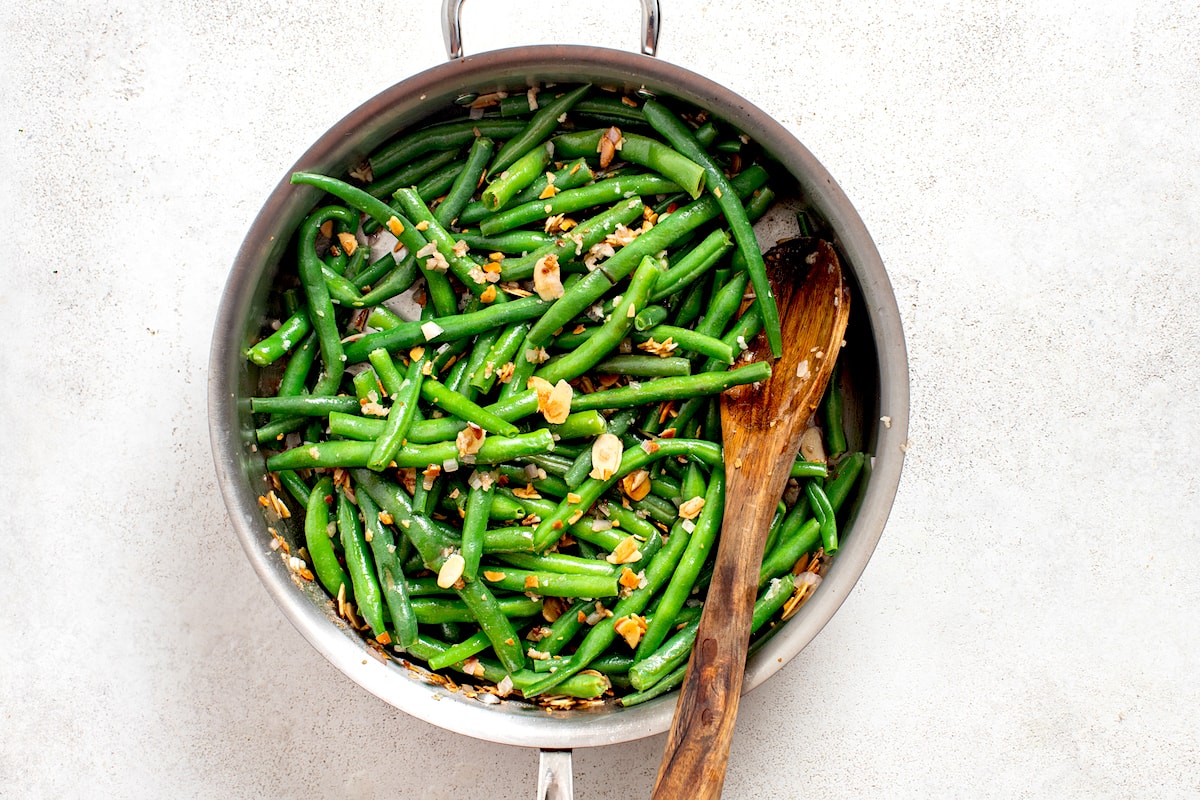 green beans almondine cooking in skillet with wooden spoon. 