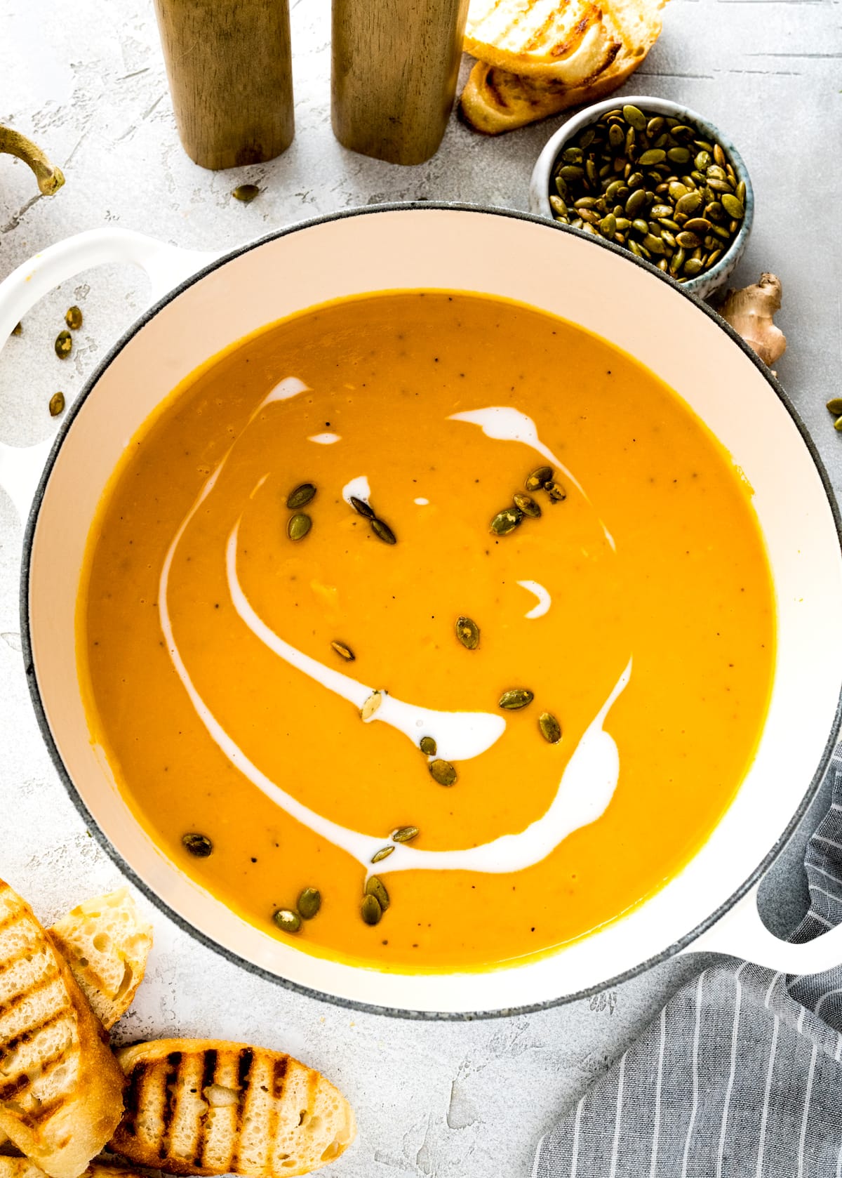 roasted butternut squash pear ginger soup in large white pot with coconut milk and pepitas. 