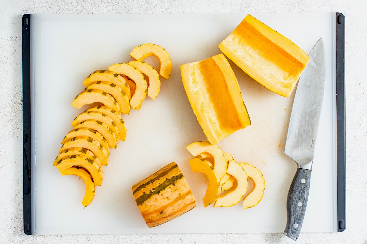 delicata squash being cut into slices with knife on cutting board. 