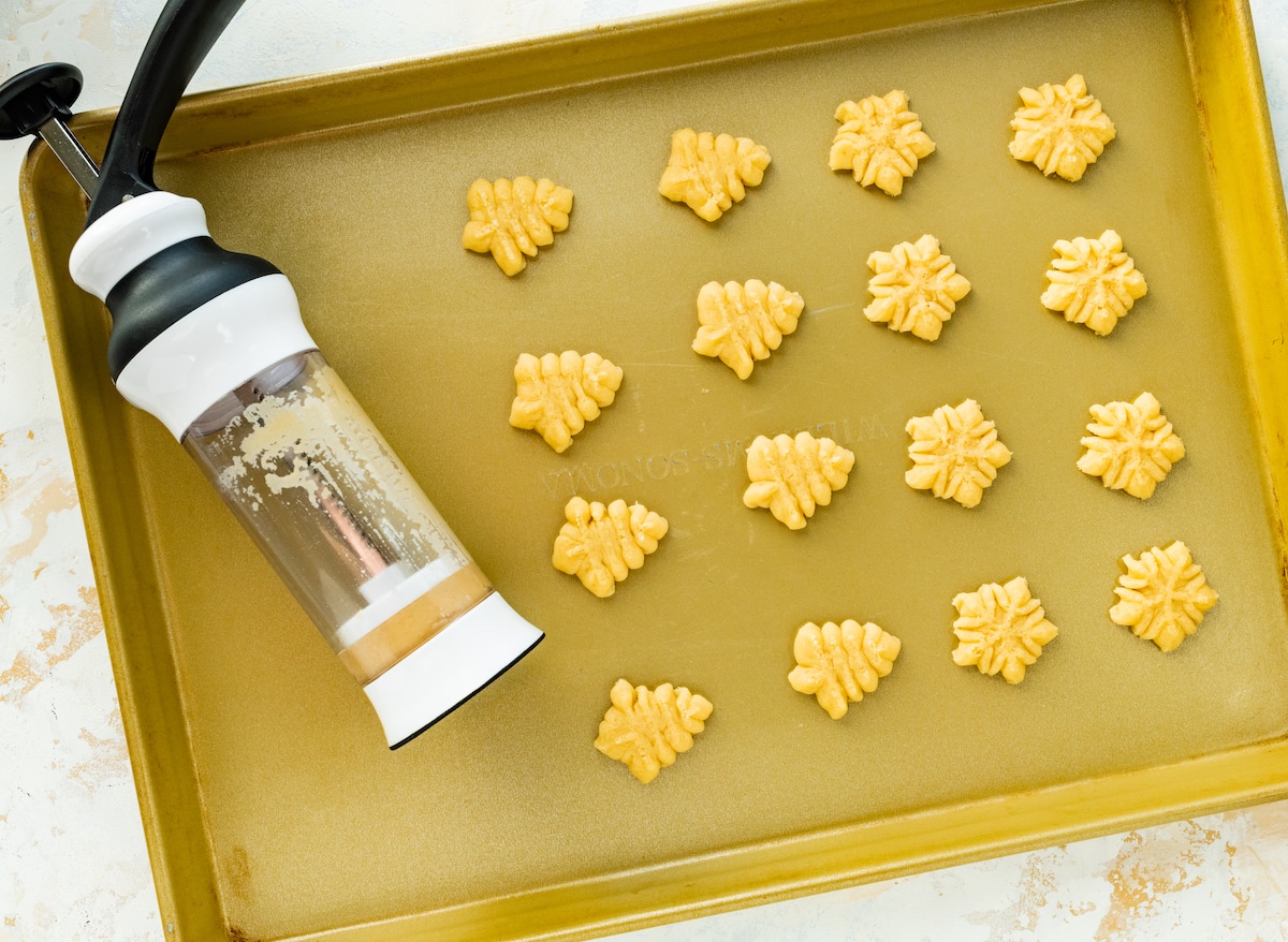 cookie press on baking sheet with spritz cookies. 