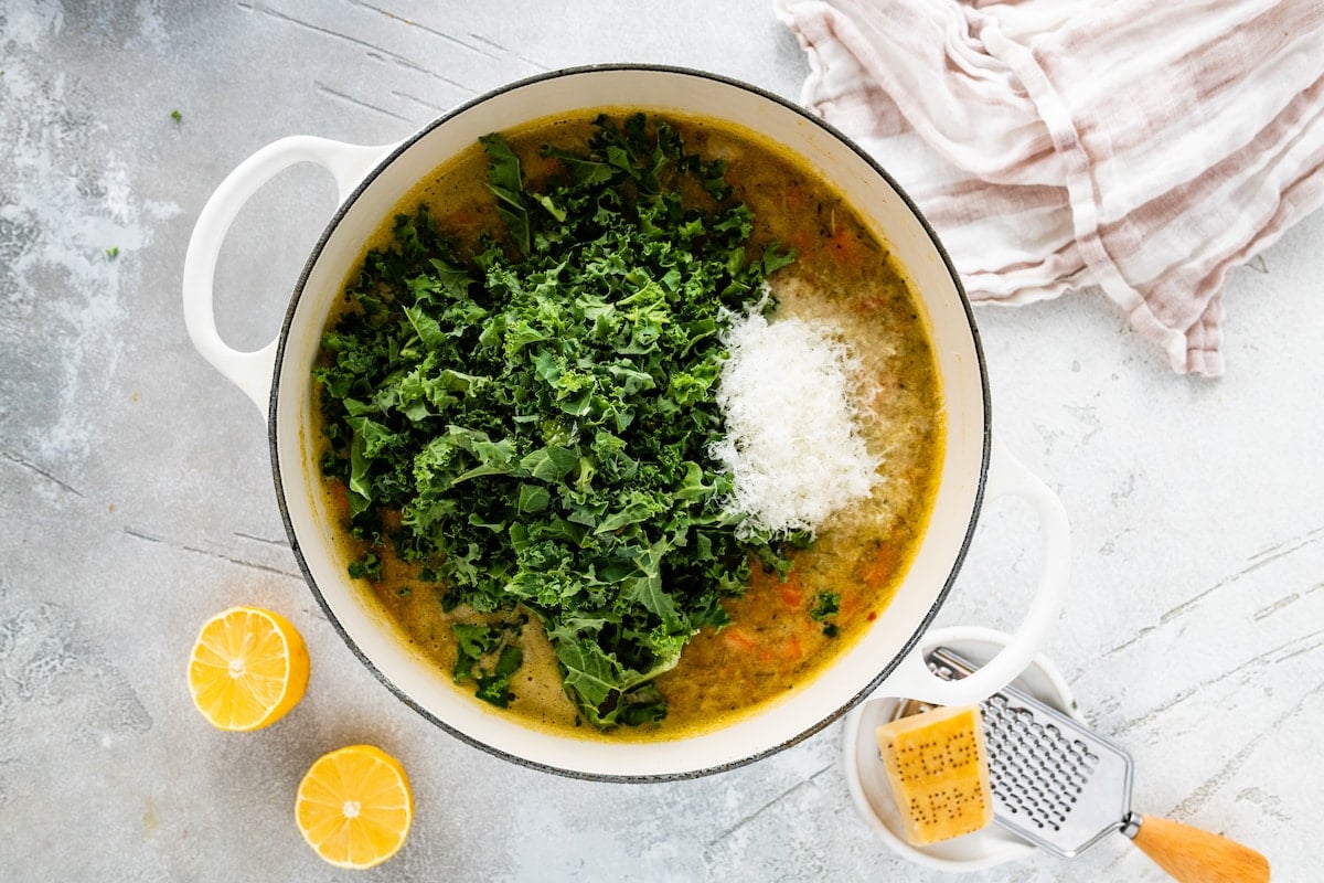 kale and parmesan cheese being added to pot of chickpea soup. 