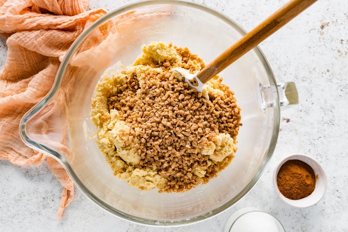 toffee bits being stirred into cookie dough in mixing bowl with spatula. 