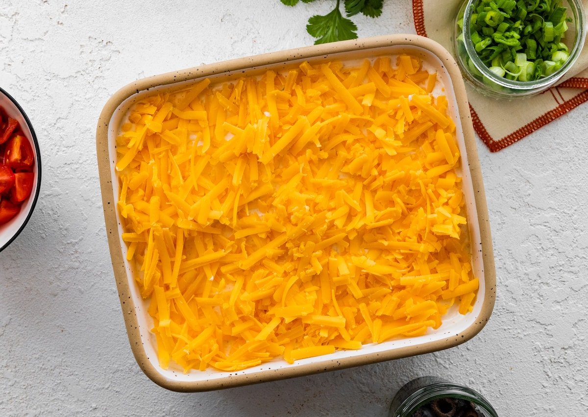 adding shredded cheese to 7 layer dip in dish. 
