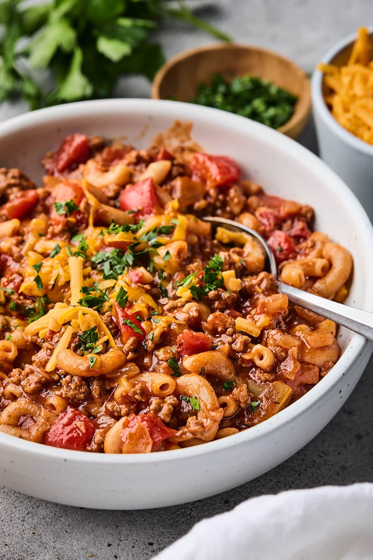 American goulash with shredded cheese in bowl with spoon. 