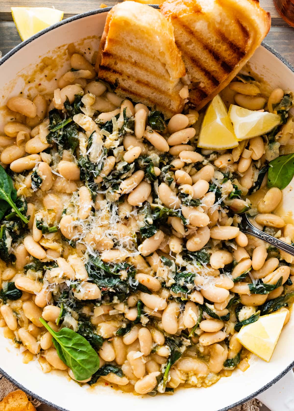 creamy white beans with spinach in skillet with Parmesan cheese and crusty bread. 