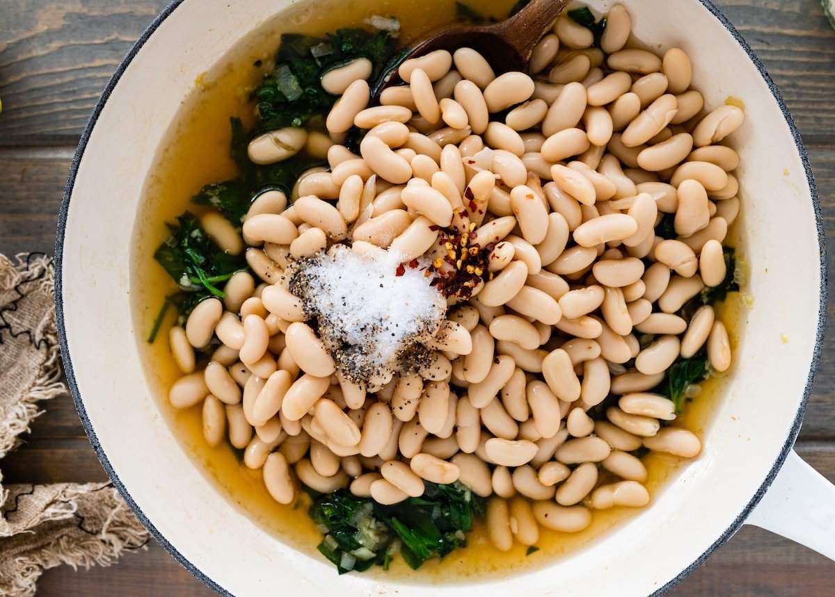 white beans in skillet with spinach, broth, crushed red pepper flakes, salt, and black pepper. 