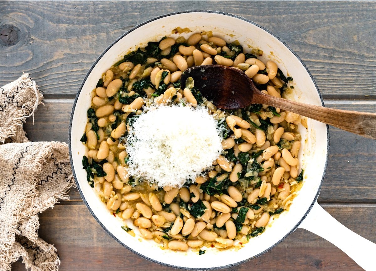 white beans and spinach in skillet with Parmesan cheese and wooden spoon. 